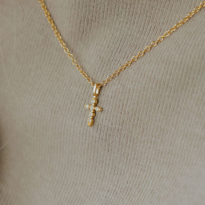 Close-up of dainty cross necklace showing delicate craftsmanship in gold.