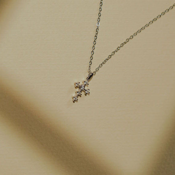 Dainty cross necklace worn on a model, showing size, shine, and minimalist design in gold and silver.