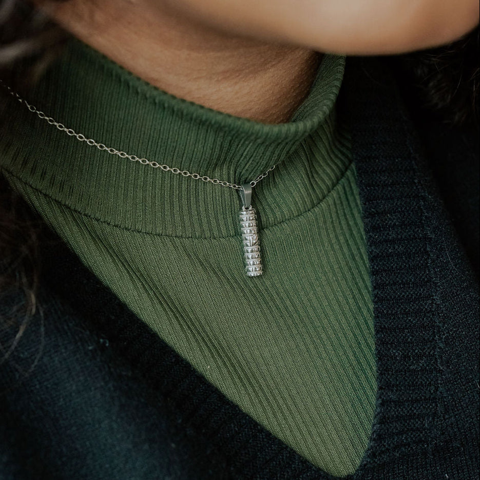 Close-up of gold Mezuzah necklace showing detailed Shin symbol and Western Wall engraving.