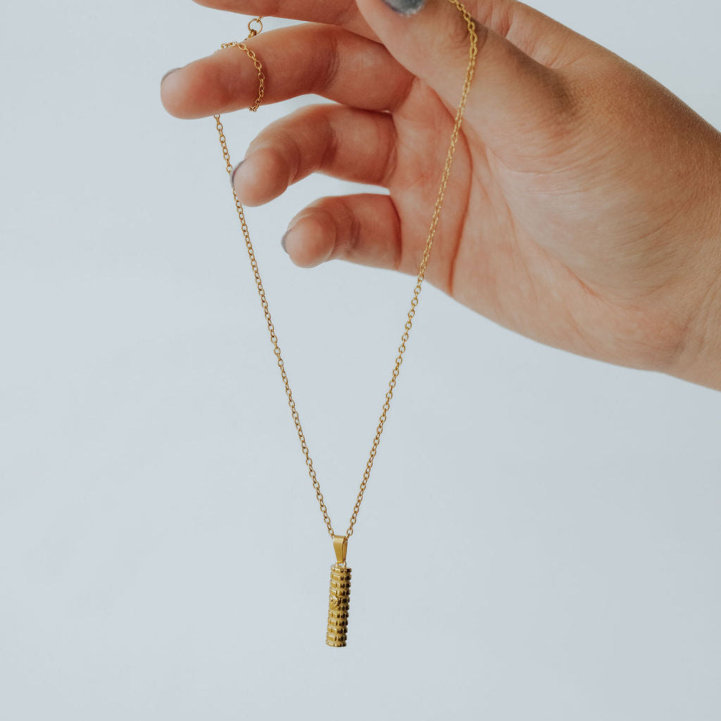 Gold or silver Mezuzah necklace worn on a model, featuring Shin symbol and Western Wall design.