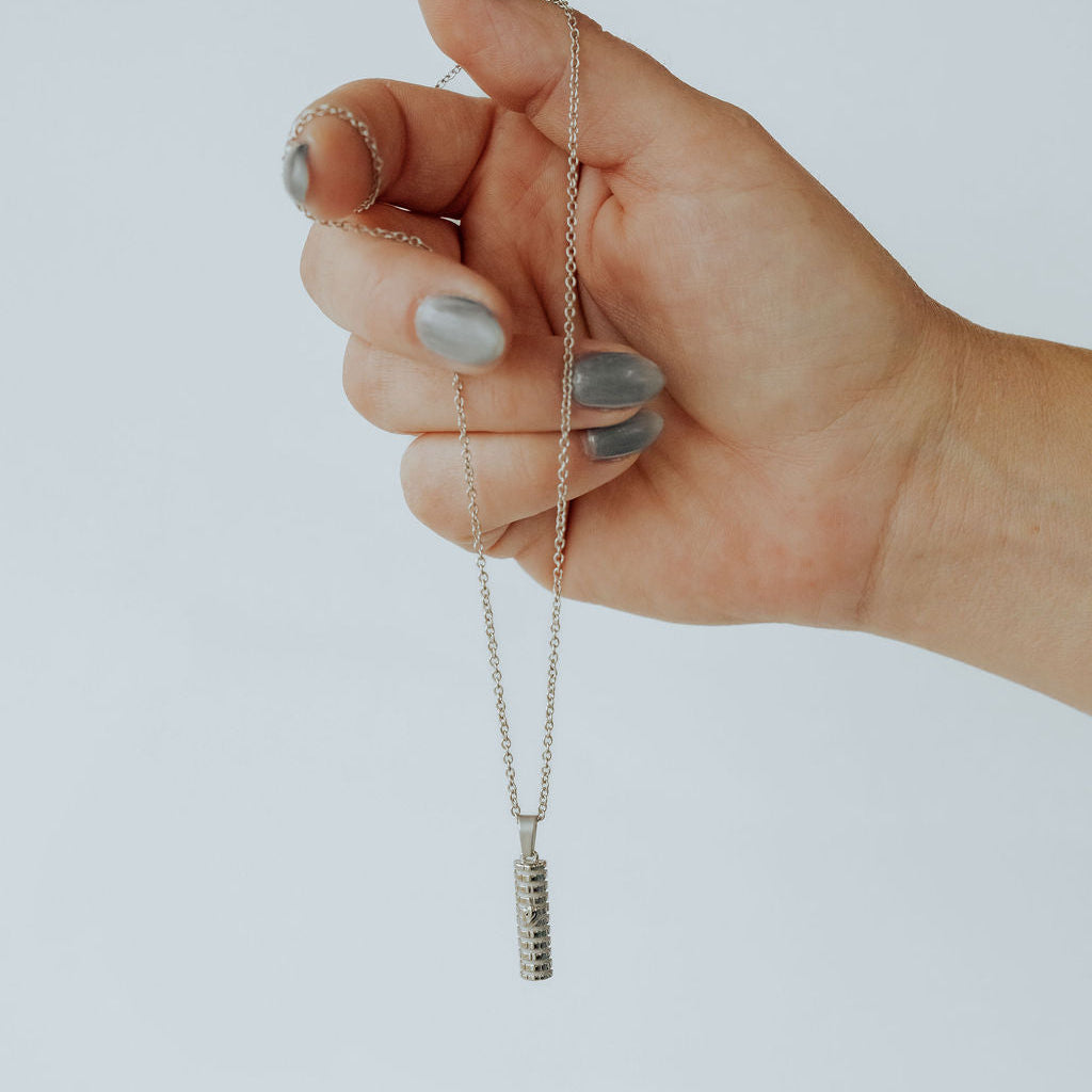 Close-up of silver Mezuzah necklace highlighting Shin symbol and Western Wall background.