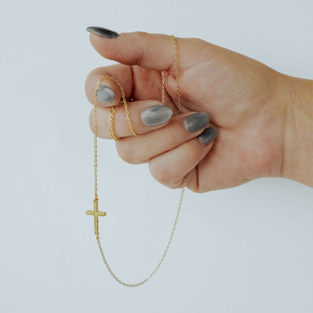 Close-up of gold sideways cross necklace, showing polished finish and horizontal design.